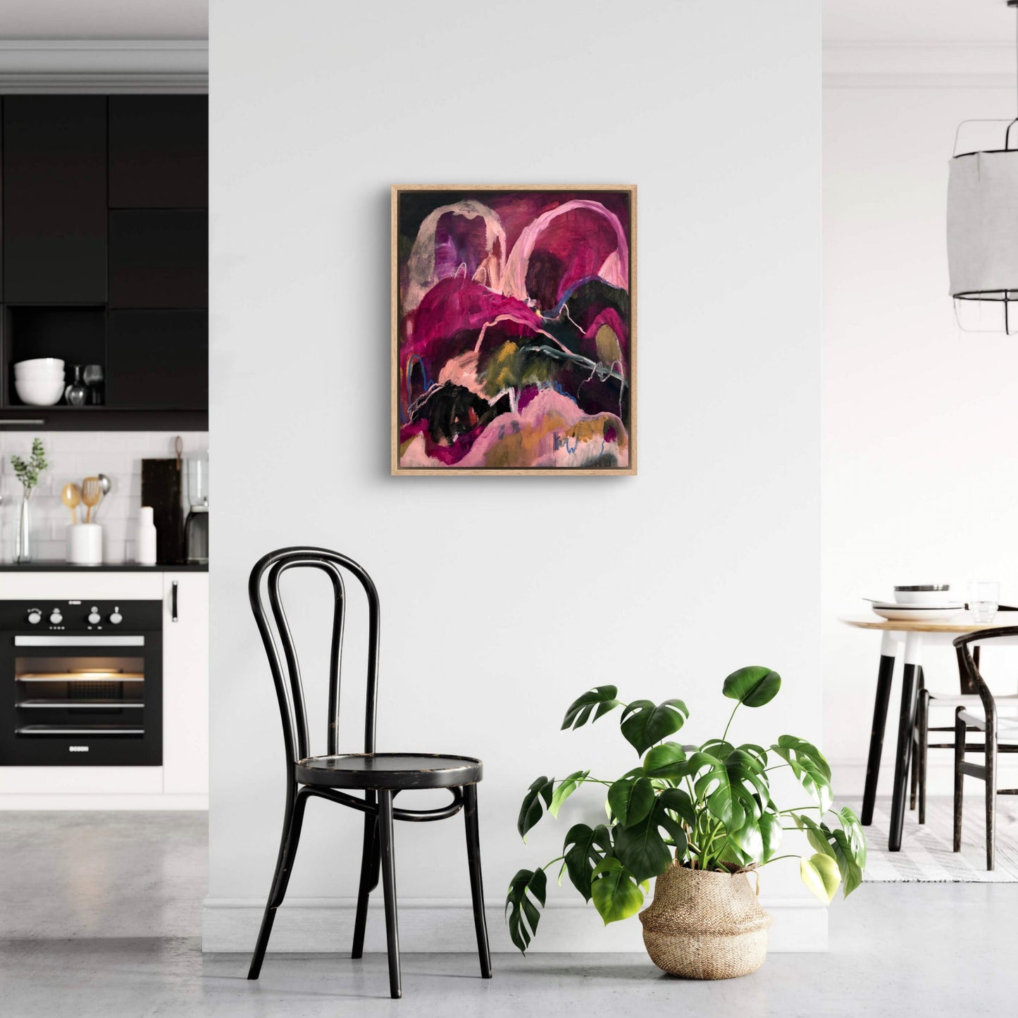Abstract landscape painting with bright pinks, dark greens and peaches, hanging in a white and black kitchen