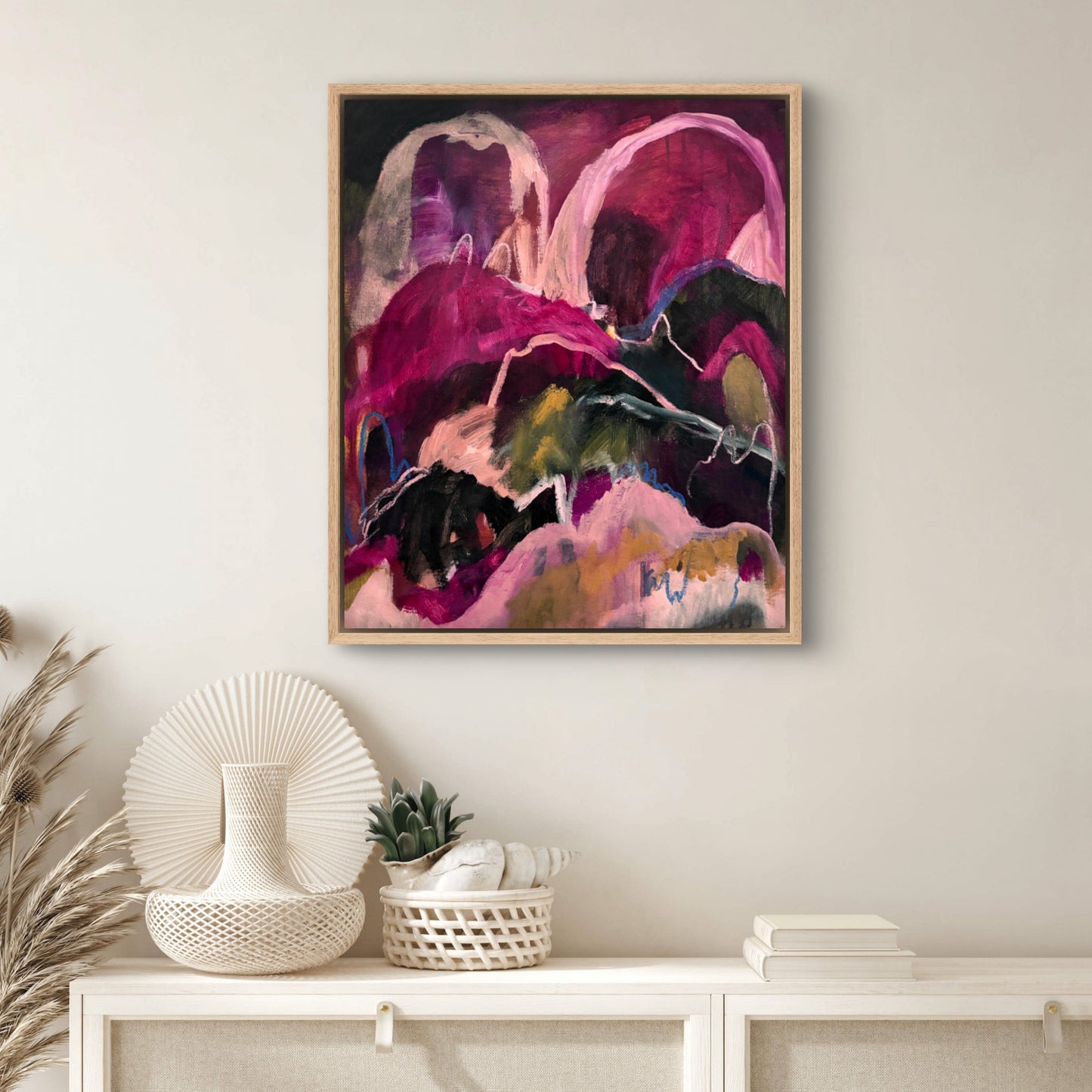 Abstract landscape painting with bright pinks, dark greens and peaches, hanging on a white wall above a hallway table with white home decor