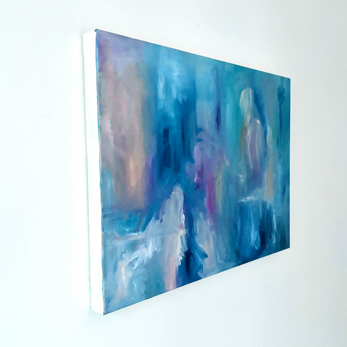 Framed original abstract painting with blue, pink, white and peach colours on a white wall at an angle
