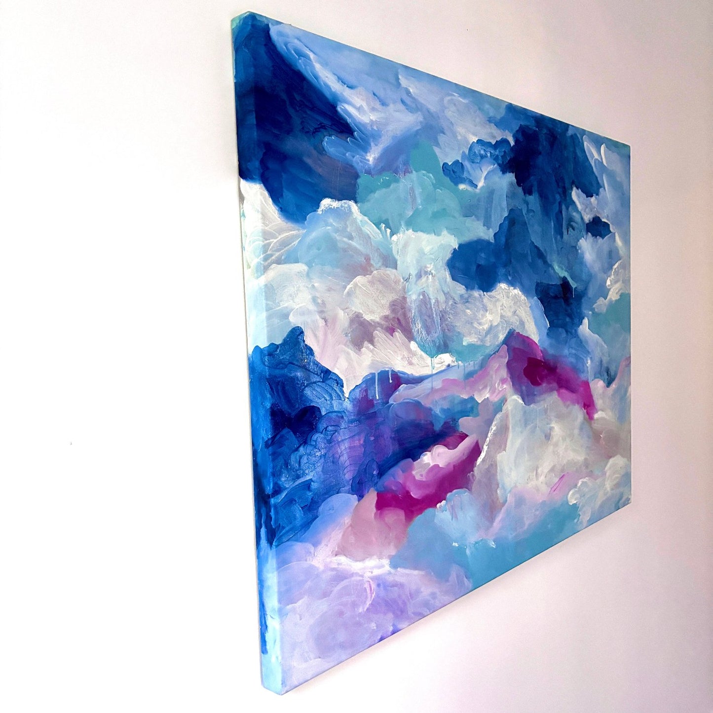 Original Cloud Painting in blue, white and pink, hanging on a white wall at a side angle