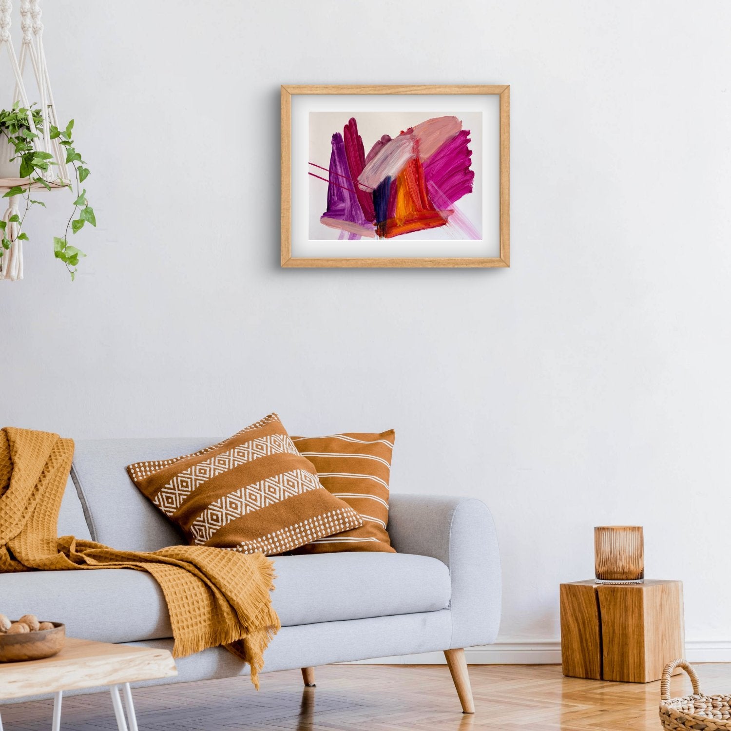 Bright expressive abstract artwprk on paper with pink, purple, orange and peach colours in an oak frame hanging above a couch with mustard cushions