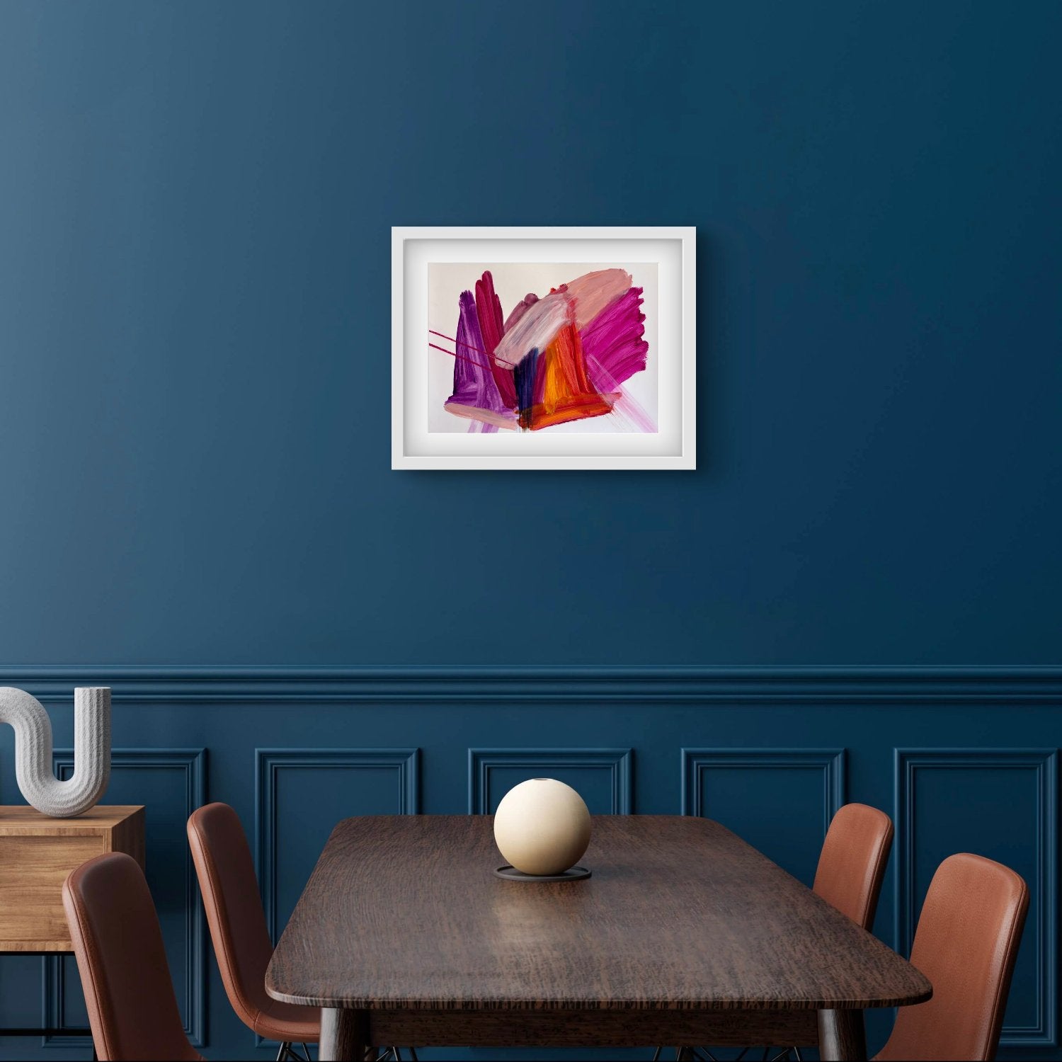 Bright expressive abstract artwprk on paper with pink, purple, orange and peach colours in a white frame hanging on a teal wall above a dining table