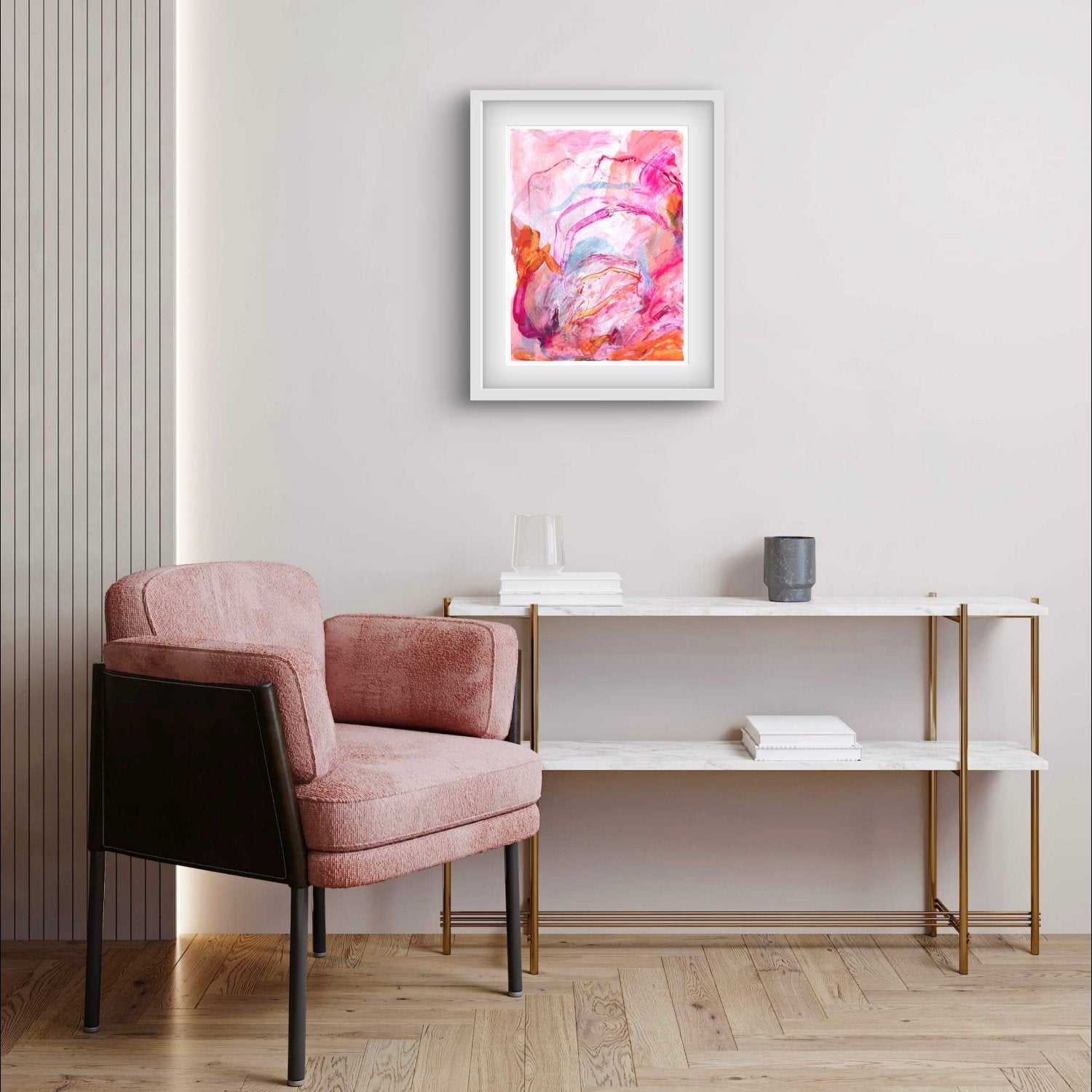 Abstract painting on paper with bright pink, orange and peach colours in a white frame hanging above a pink chair