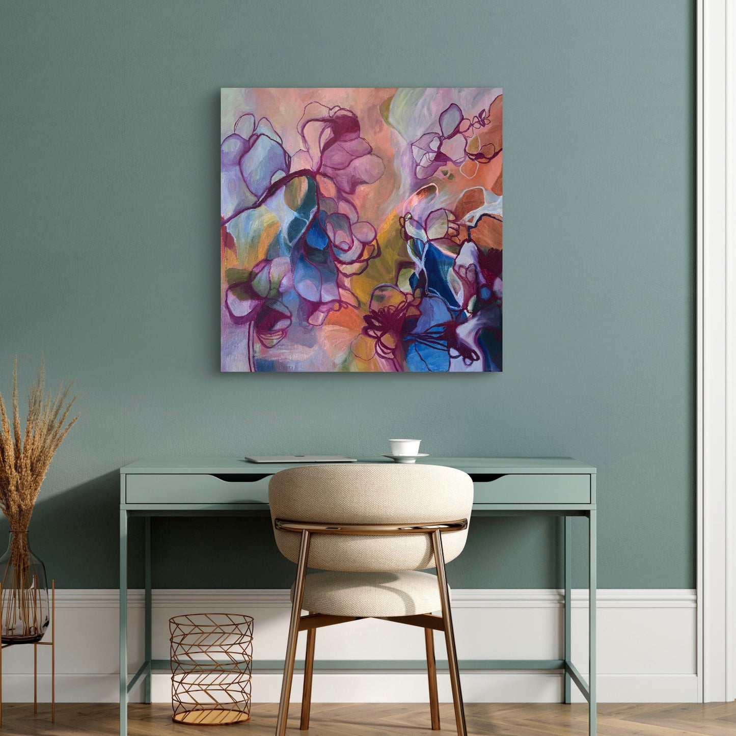 An abstract canvas art print with vibrant purple, pink, orange, and blue brushstrokes, displayed on a sage green wall above a modern desk and chair.