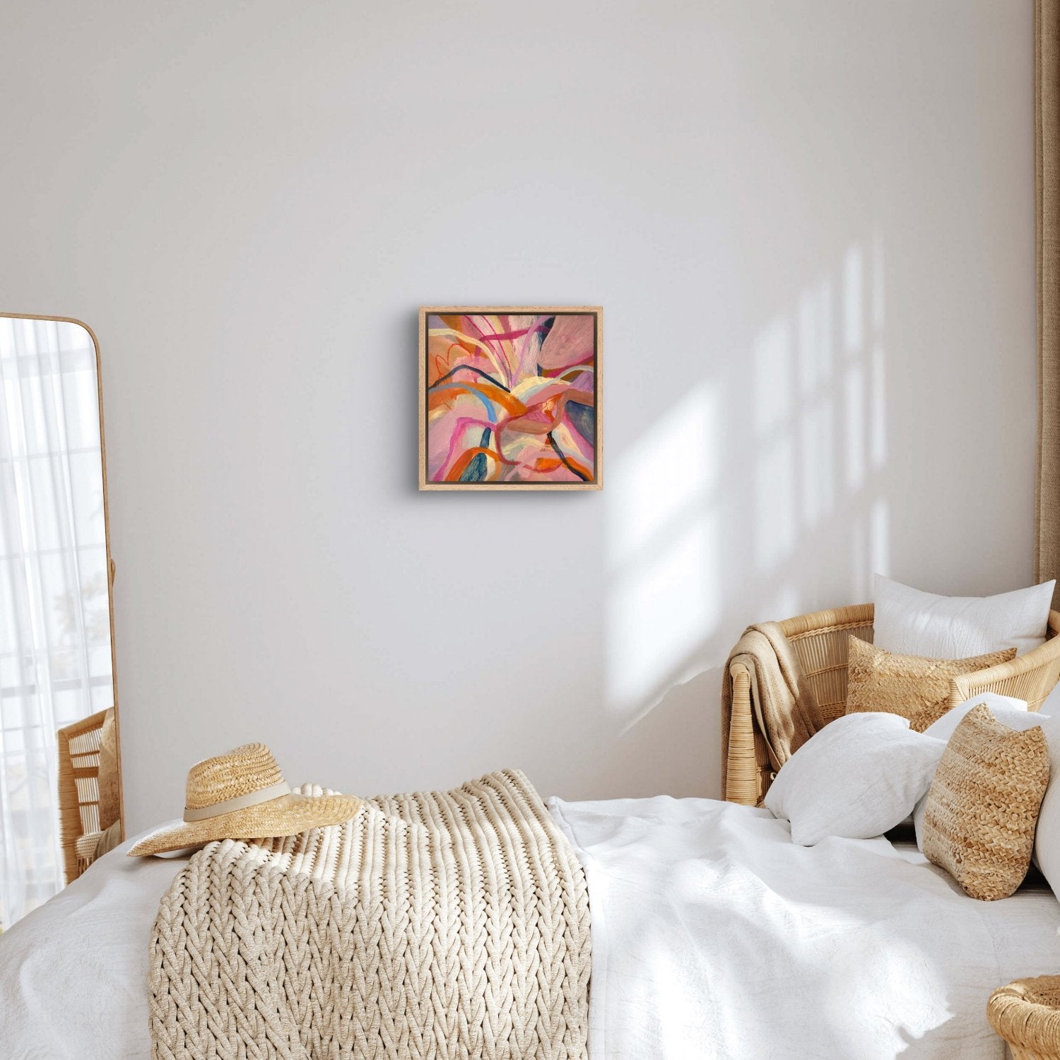abstract acrylic painting with birght pink, orange and blue colours in an oak frame hanging in a white bedroom