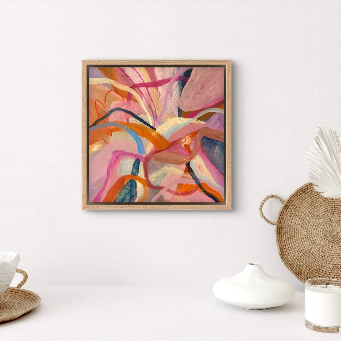 abstract acrylic painting with birght pink, orange and blue colours in an oak frame hanging on a white wall above homeware objects