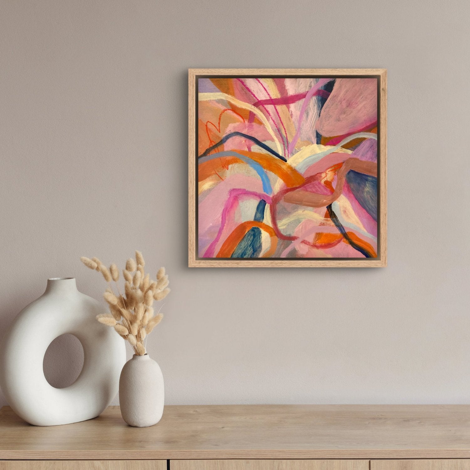 abstract acrylic painting with birght pink, orange and blue colours in an oak frame haning above a hallway table with white vases