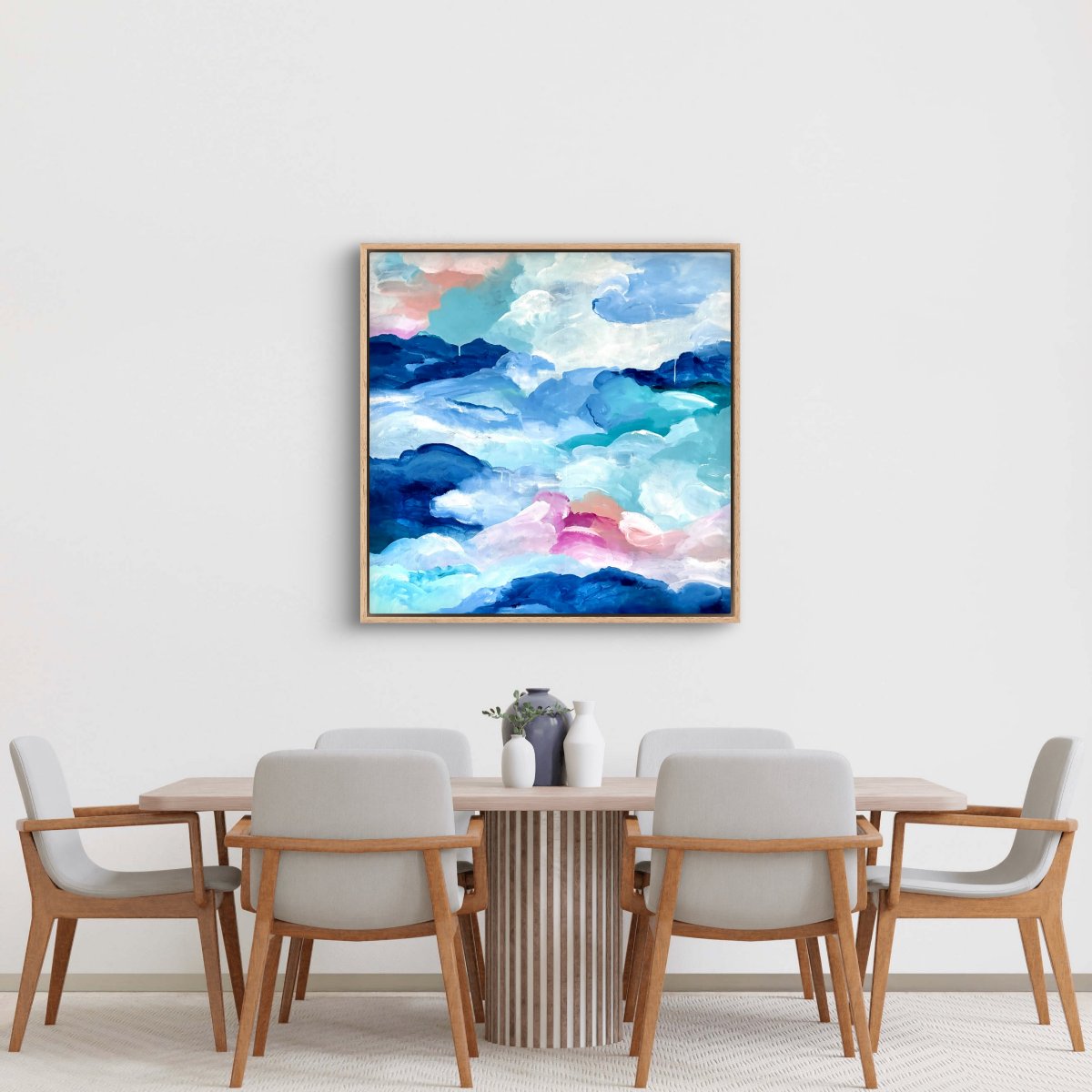 Framed original artwork of abstract clouds of blue, green, white and peach on a neutral background in front of a dining table