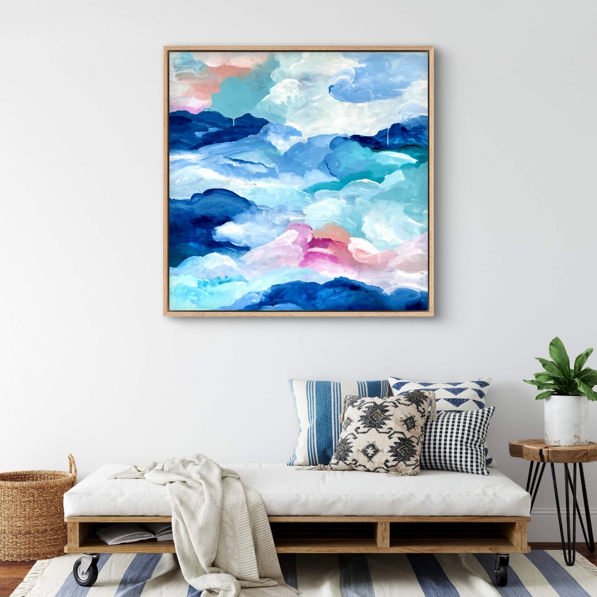 Framed original artwork of abstract clouds of blue, green, white and peach on a neutral background with a day bed in front with blue cushions