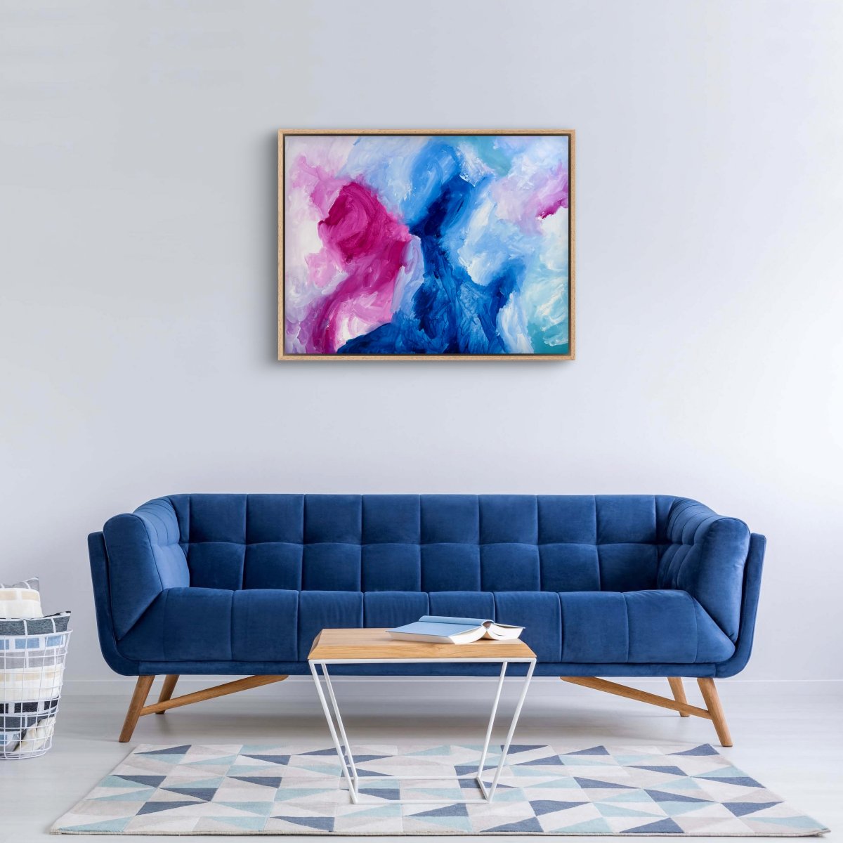 Framed original abstract painting with blue, pink and white colours on a neutral background hanging above a blue couch