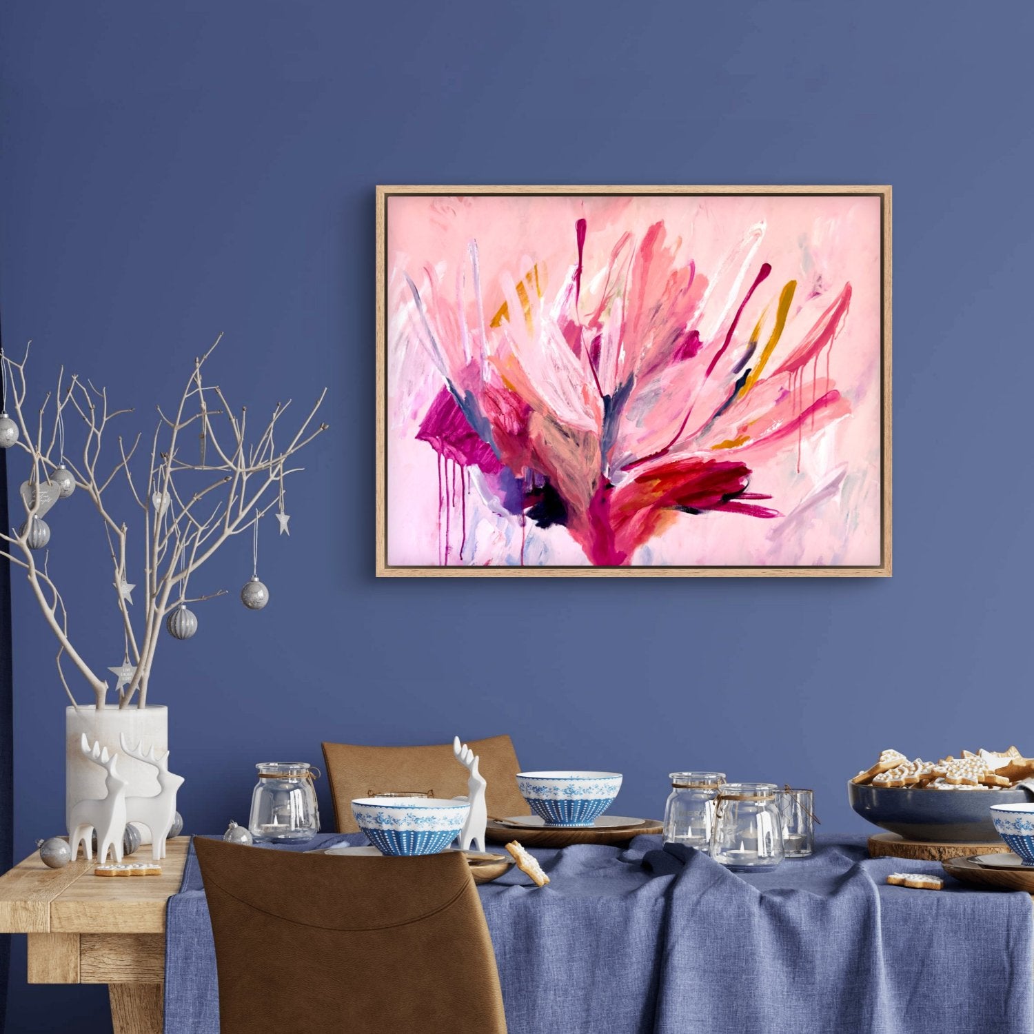 A large botanical abstract acrylic painting with bright pink colours hanging on a blue wall in front of a dining table