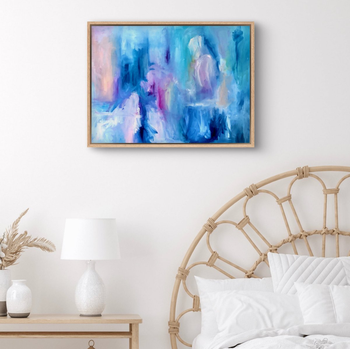 Framed original abstract painting with blue, pink, white and peach colours on a white wall behind a white bed