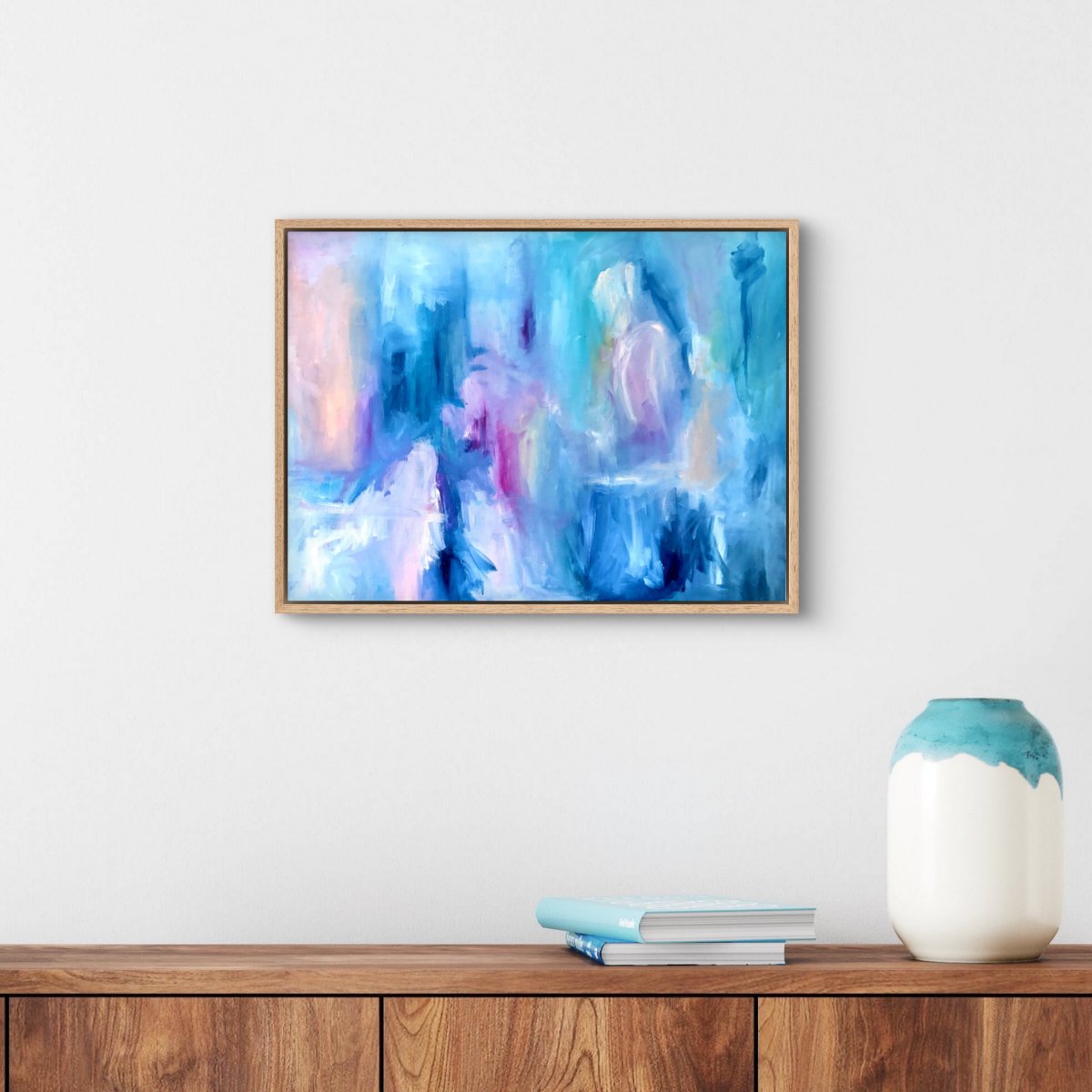Framed original abstract painting with blue, pink, white and peach colours on a white wall above a hallway table