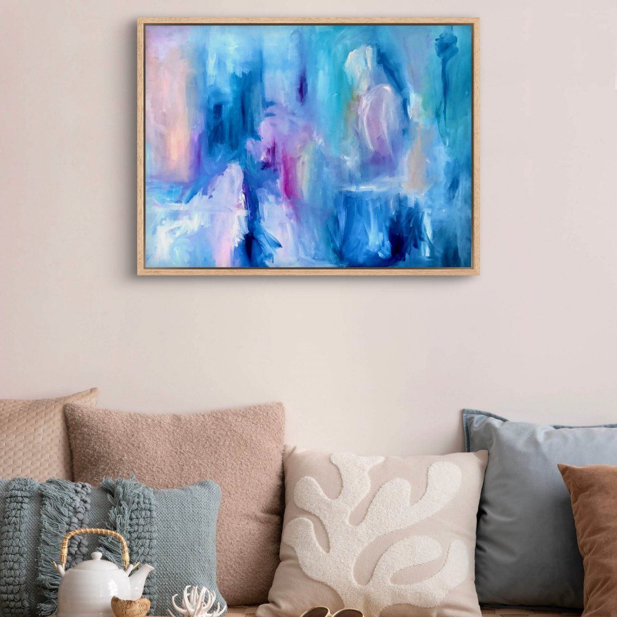 Framed original abstract painting with blue, pink, white and peach colours on a white wall above a daybed with cushions