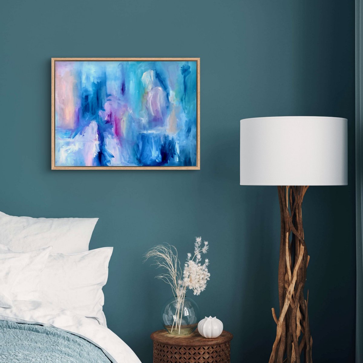 Framed original abstract painting with blue, pink, white and peach colours on a teal wall behind a bed 