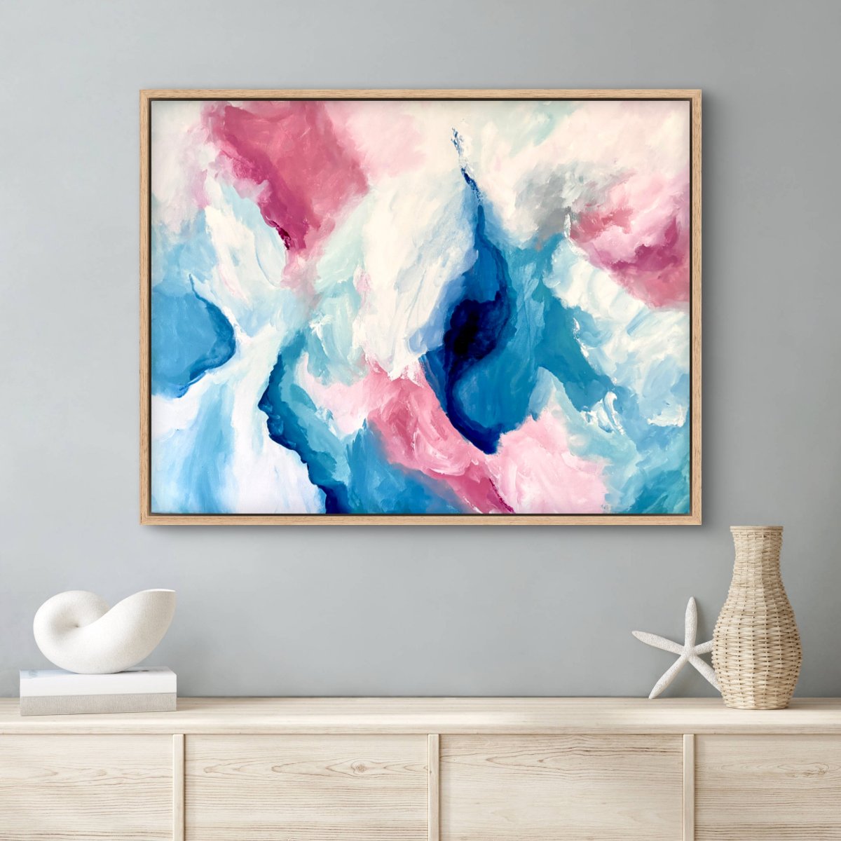 Framed original painting of abstract clouds in blue, green, peach and white hanging above a hallway table with beach objects