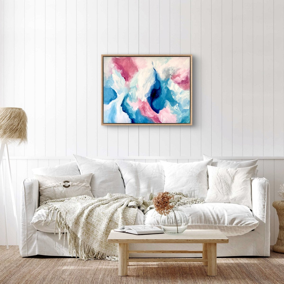Framed original painting of abstract clouds in blue, green, peach and white hanging on a white wall in a lounge room with a white sofa