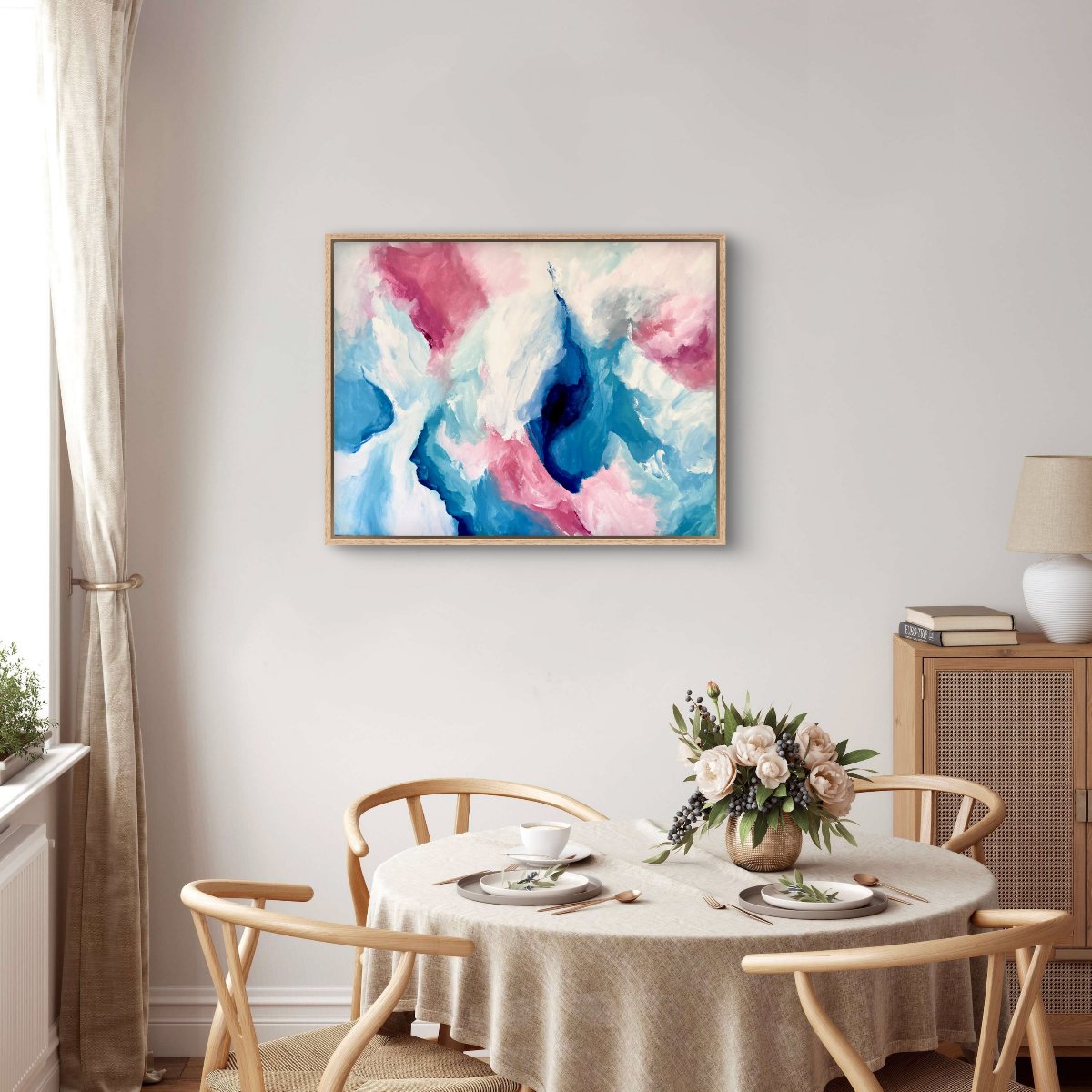 Framed original painting of abstract clouds in blue, green, peach and white in a dining room with a neutral table and linens