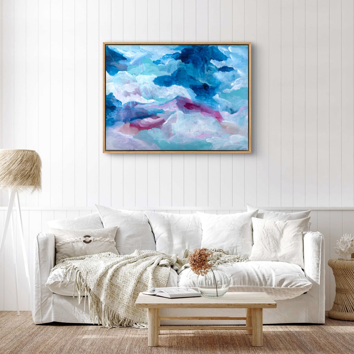 Original painting of abstract clouds in blue, white and pink, hanging on a white wall with a cream couch in front
