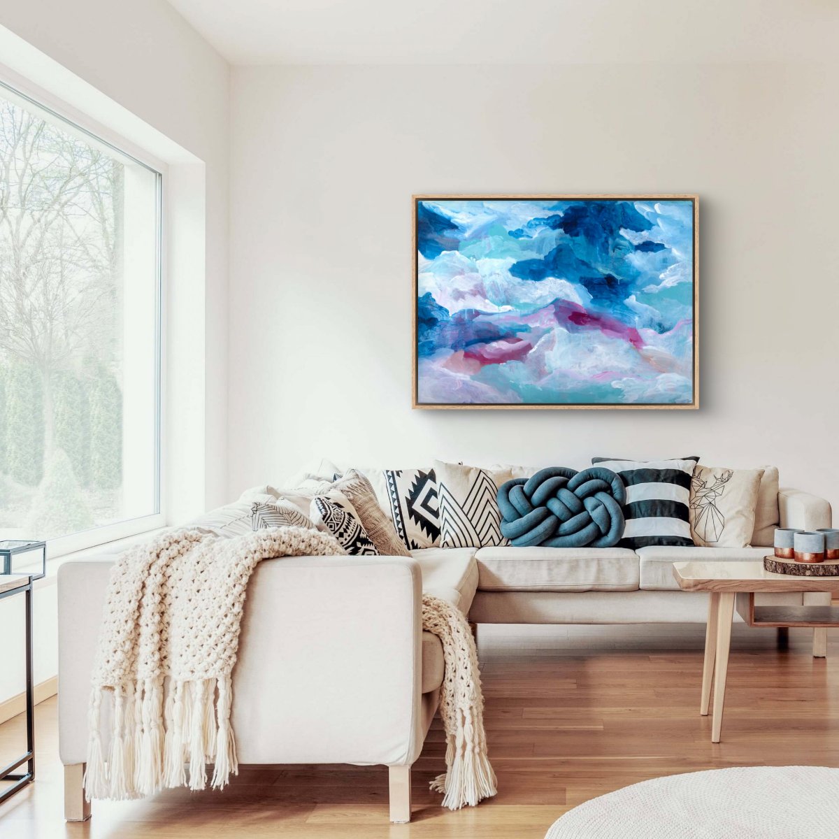 Original painting of abstract clouds in blue, white and pink in an oak frame in a cream lounge room with a cream couch and teal cushions