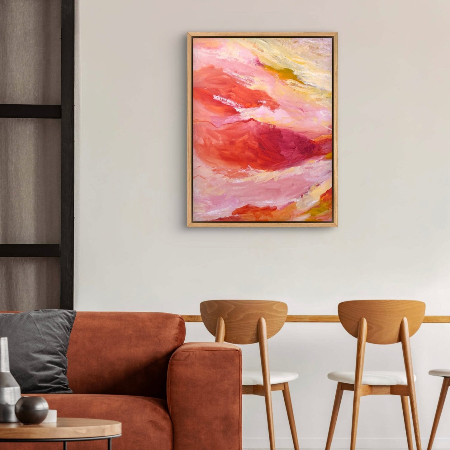 large abstract landscape painting with orange, pink and yellow colours hanging on a white wall above a brown couch